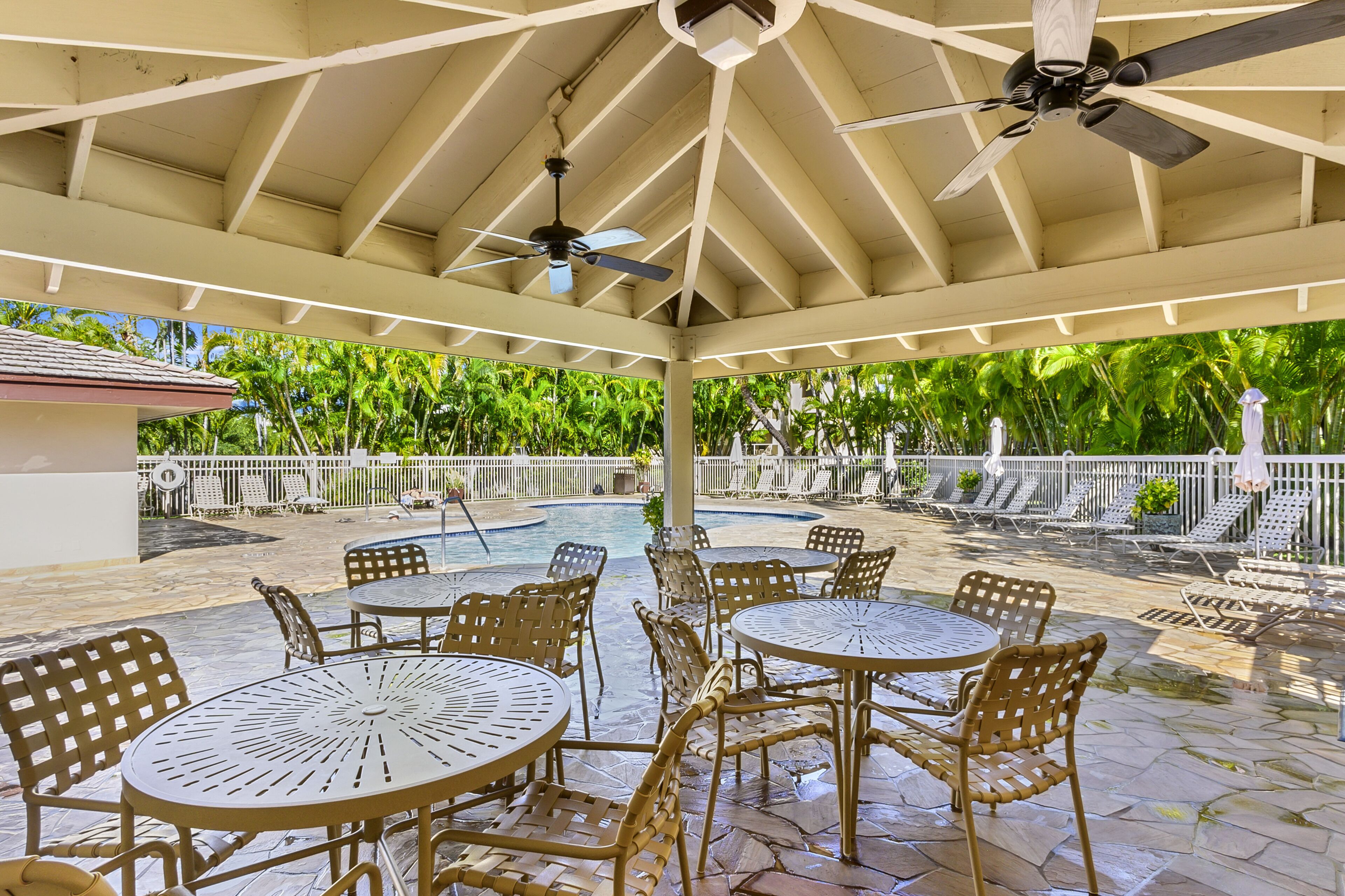 A covered outdoor area with tables and chairs, a pool, and a ceiling fan.