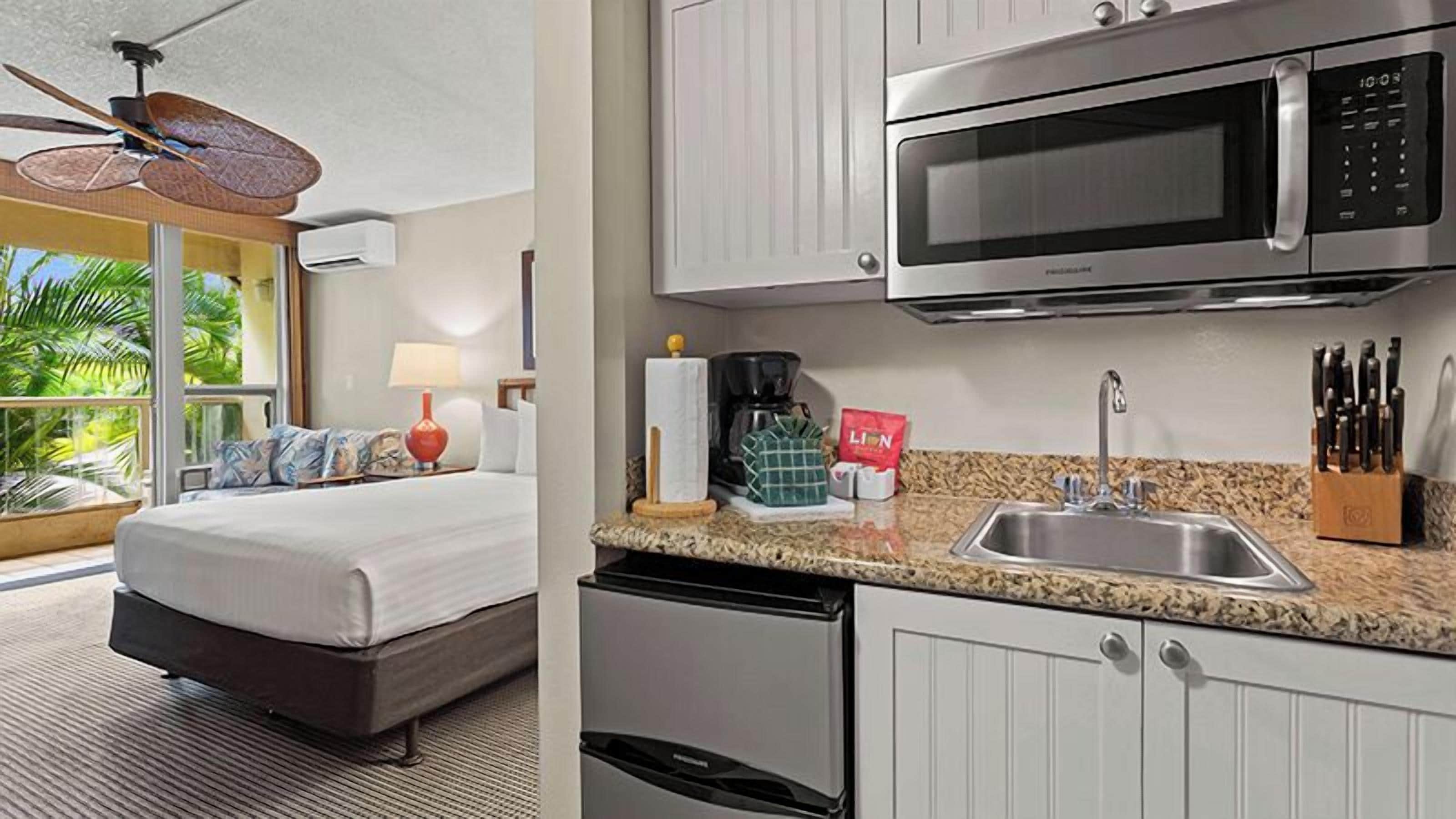 A hotel room with a bed, a kitchenette with a microwave, a sink, and a view of the outdoors.