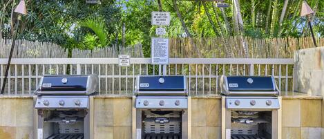 Three barbecue grills against a bamboo fence with a sign prohibiting glass containers.