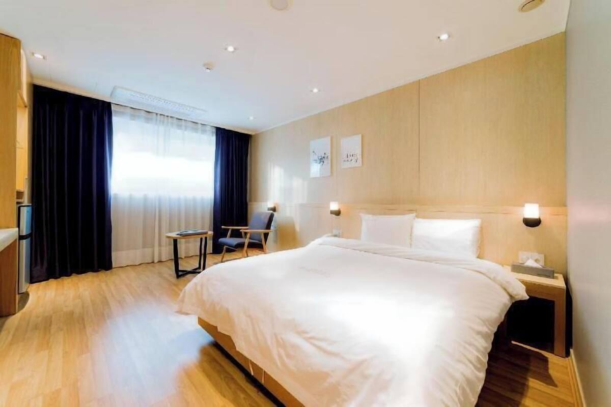 A hotel room with a large bed, a chair, a desk, and a window with curtains.