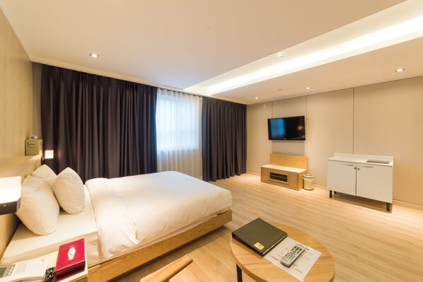 Habitación de hotel moderna con una cama grande, un escritorio con una computadora portátil, un televisor y un armario.