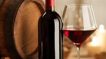 Uma garrafa e um copo de vinho sobre uma superfície de madeira, com um barril ao fundo.