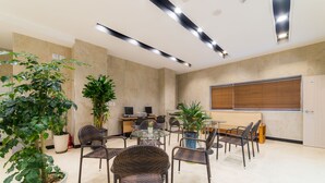 A modern conference room with a glass table, wicker chairs, potted plants, and a large window with blinds. - Reborn Suwon Silkroad Hotel (Suwon)