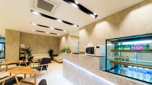 A modern hotel lobby with a reception desk, seating area, and a glass display case with bottled water. - Reborn Suwon Silkroad Hotel (Suwon)