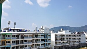 A multi-story hotel with balconies and air conditioning units, set against a backdrop of mountains and clear skies. - Green Harbor Hotel & Service Apartment (Patong)