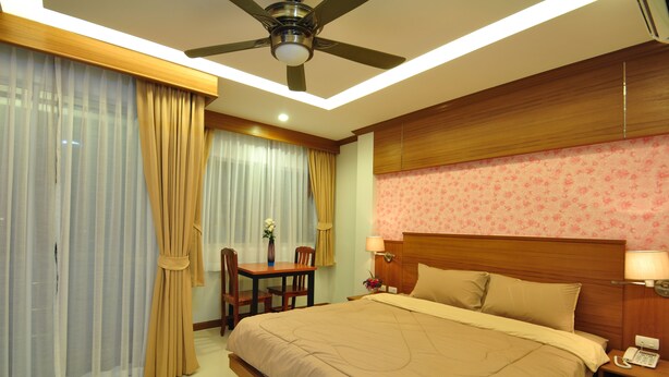 A hotel room with a large bed, a desk with a chair, a ceiling fan, and a telephone on the nightstand. - Green Harbor Hotel & Service Apartment (Patong)
