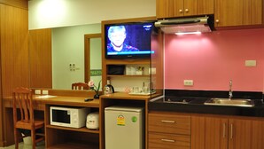 A compact kitchenette with a microwave, refrigerator, sink, and a television displaying a program. - Green Harbor Hotel & Service Apartment (Patong)