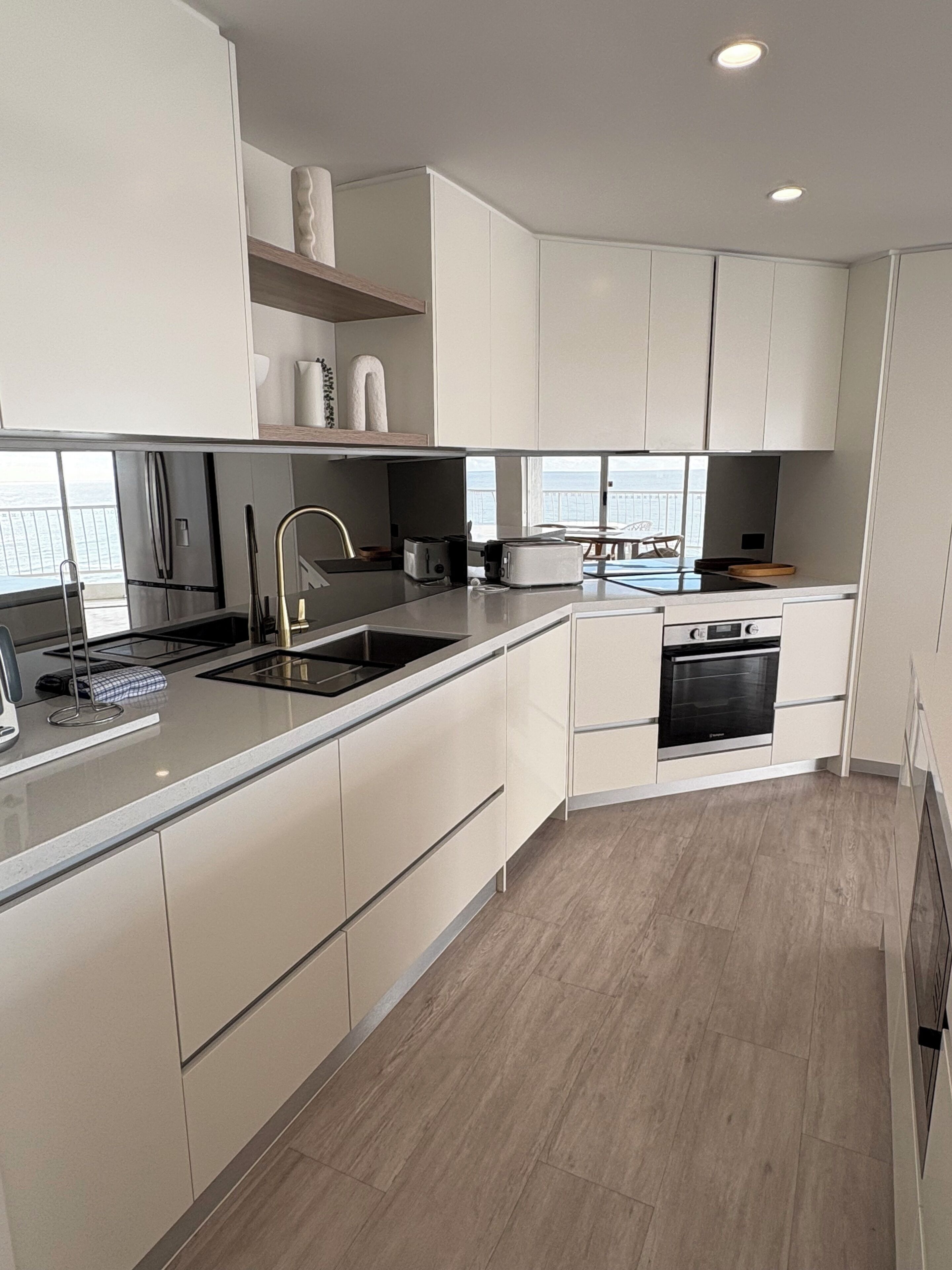 Una cocina moderna con armarios blancos, un lavamanos de acero inoxidable y un horno empotrado.