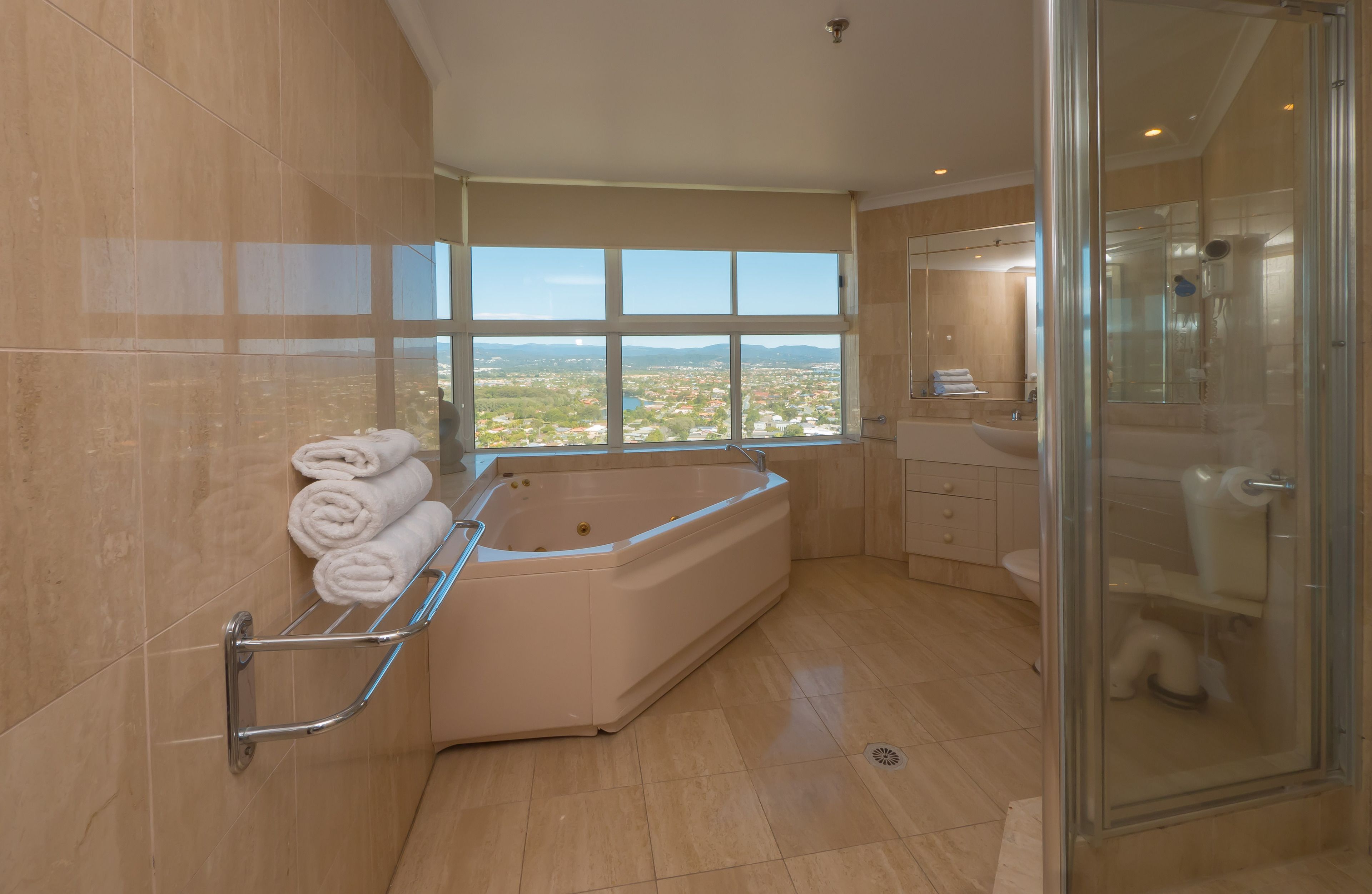 A modern bathroom with a large bathtub, a glass shower enclosure, and a view of a cityscape through a large window.