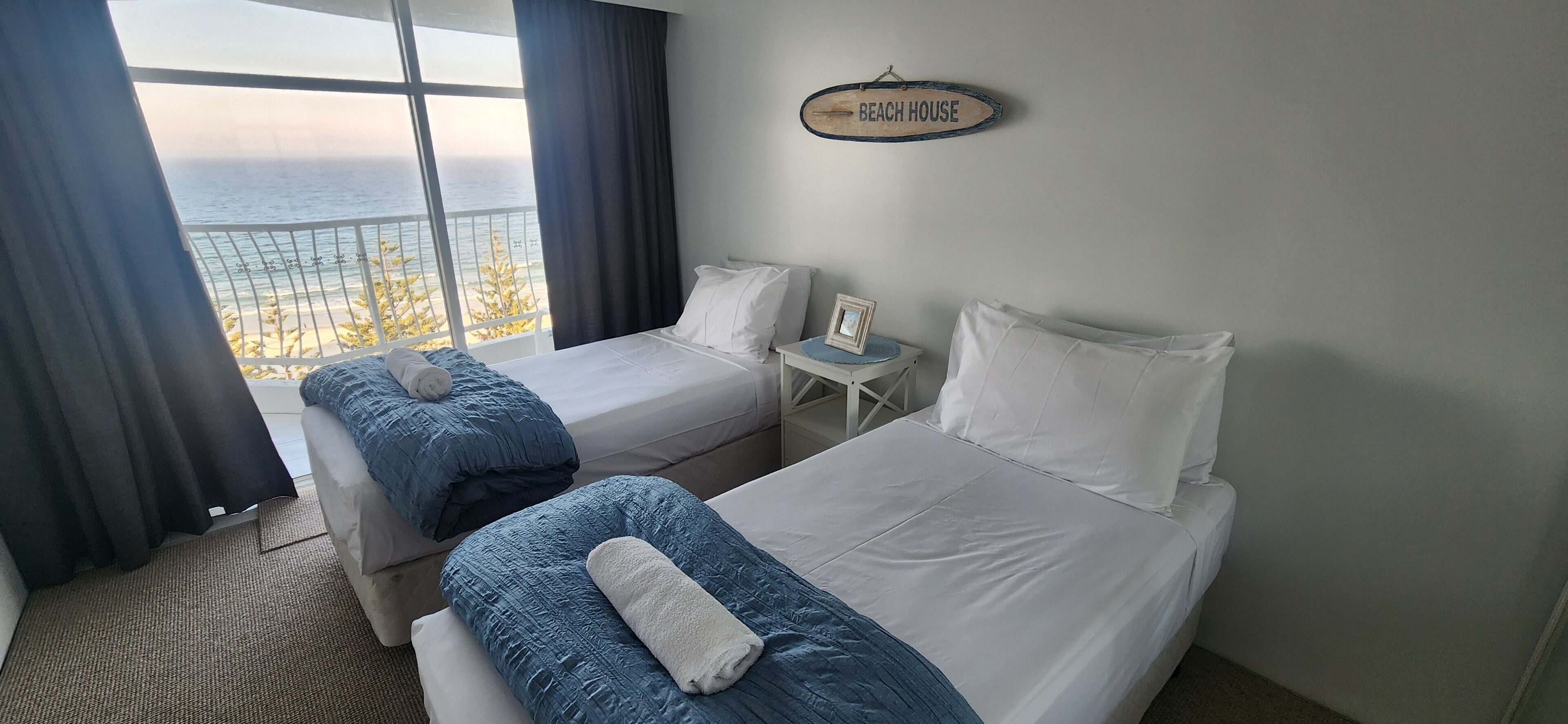 A hotel room with two beds, a view of the beach, and a sign that reads "BEACH HOUSE".
