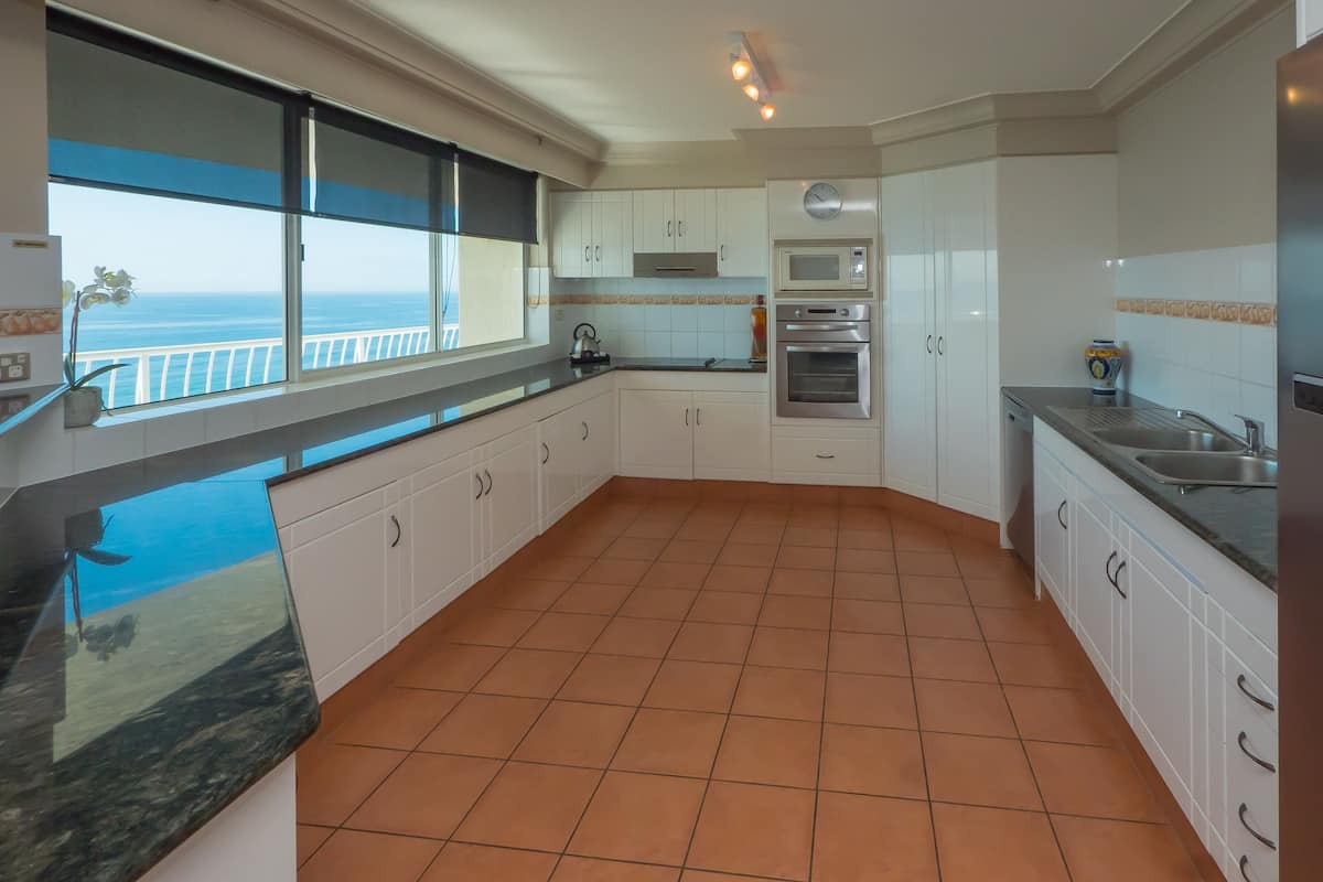 A modern kitchen with white cabinets, a stainless steel refrigerator, and a view of the ocean through a large window.