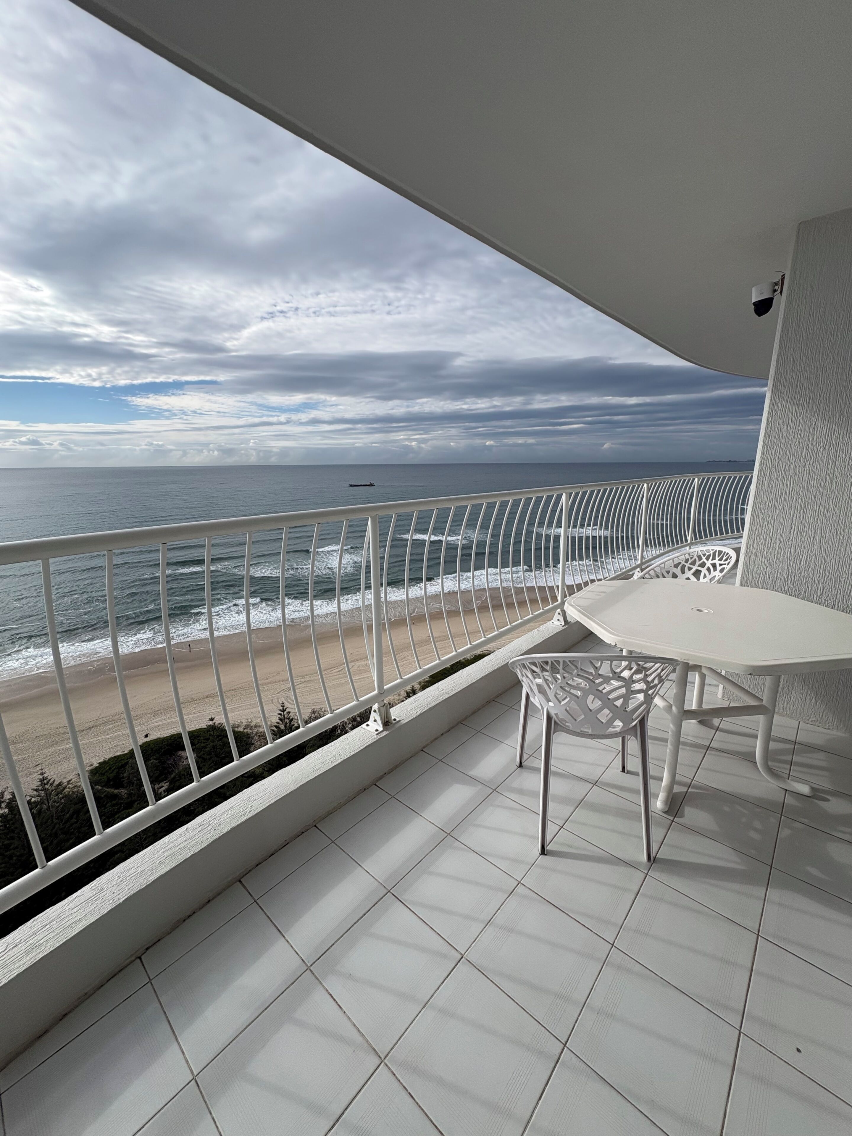 Un balcón con vista al mar, una mesa blanca y una silla blanca.