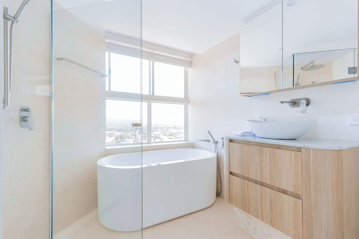 A modern bathroom with a freestanding bathtub, a large window, and a wooden vanity.
