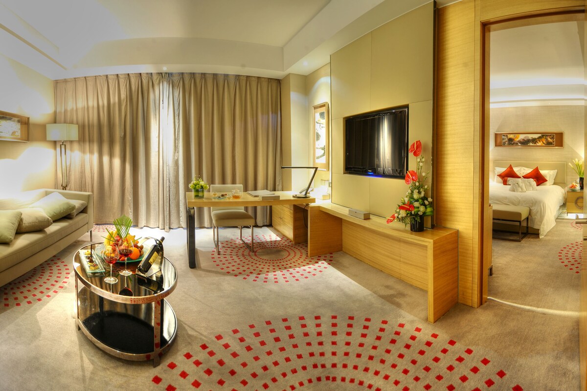 A modern hotel room with a sofa, a desk, a TV, and a bed.