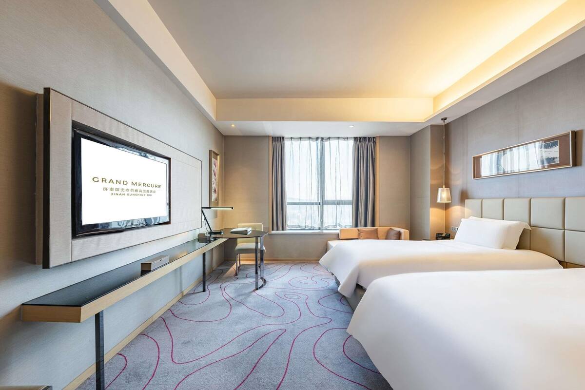 Ein Hotelzimmer mit Bett, Schreibtisch, Stuhl, Fernseher und Fenster.
