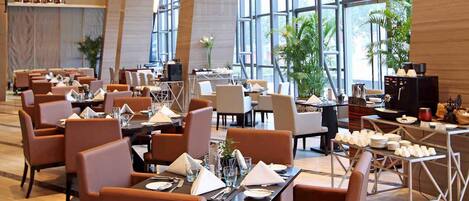 A modern restaurant with leather chairs, tables set for dining, and large windows offering views.