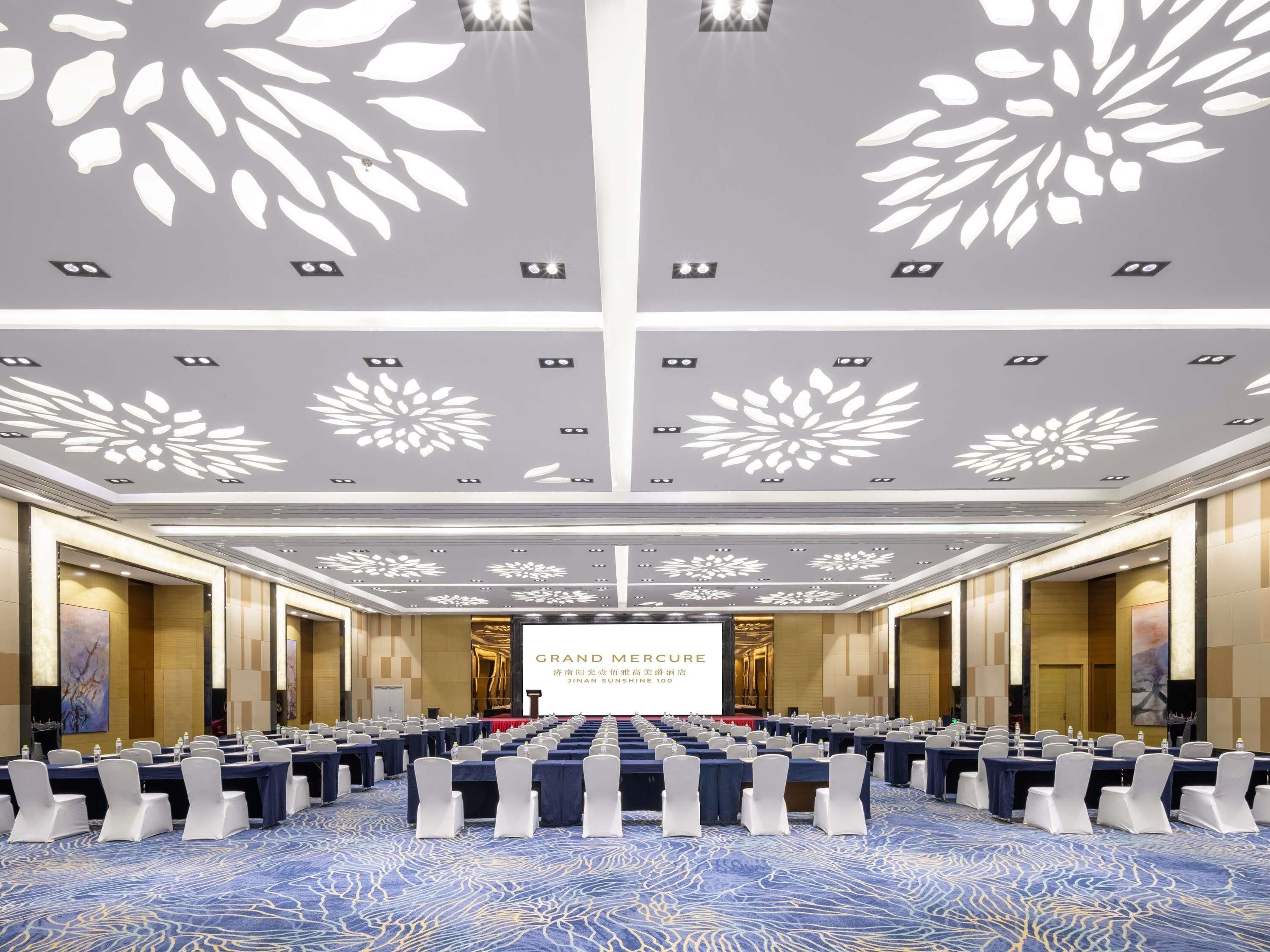Une salle de conférence équipée d’une scène, de rangées de tables et de chaises.