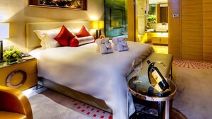 Ein Hotelzimmer mit einem großen Bett, roten Kissen, einem Nachttisch mit Flasche und Glas sowie einem Sessel.