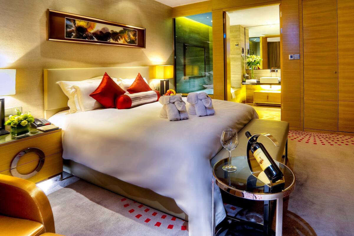 Ein Hotelzimmer mit einem großen Bett, roten Kissen, einem Nachttisch mit Flasche und Glas sowie einem Sessel.