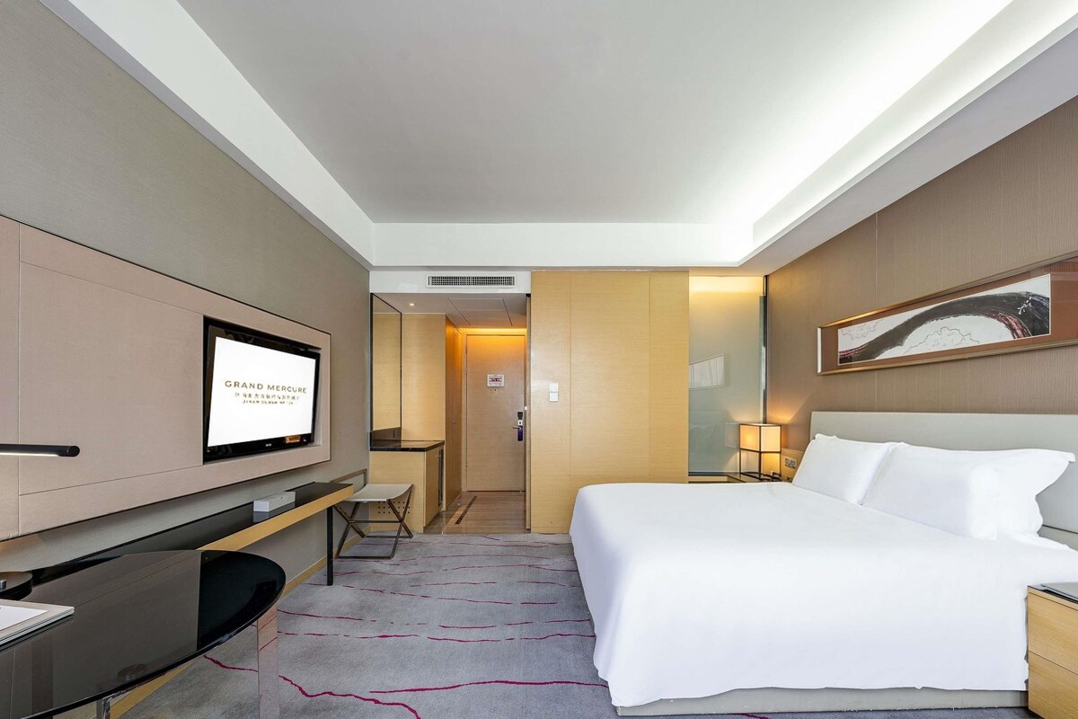 A hotel room with a bed, a desk, a TV, and a door leading to a bathroom.