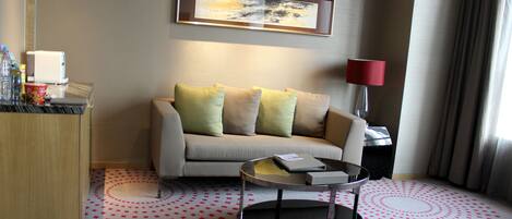 A modern hotel room with a sofa, a small round table, a lamp, and a painting on the wall.
