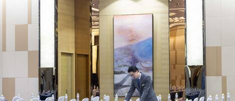 A conference room with tables set for a meeting, a large abstract painting on the wall, and a person adjusting the table settings.