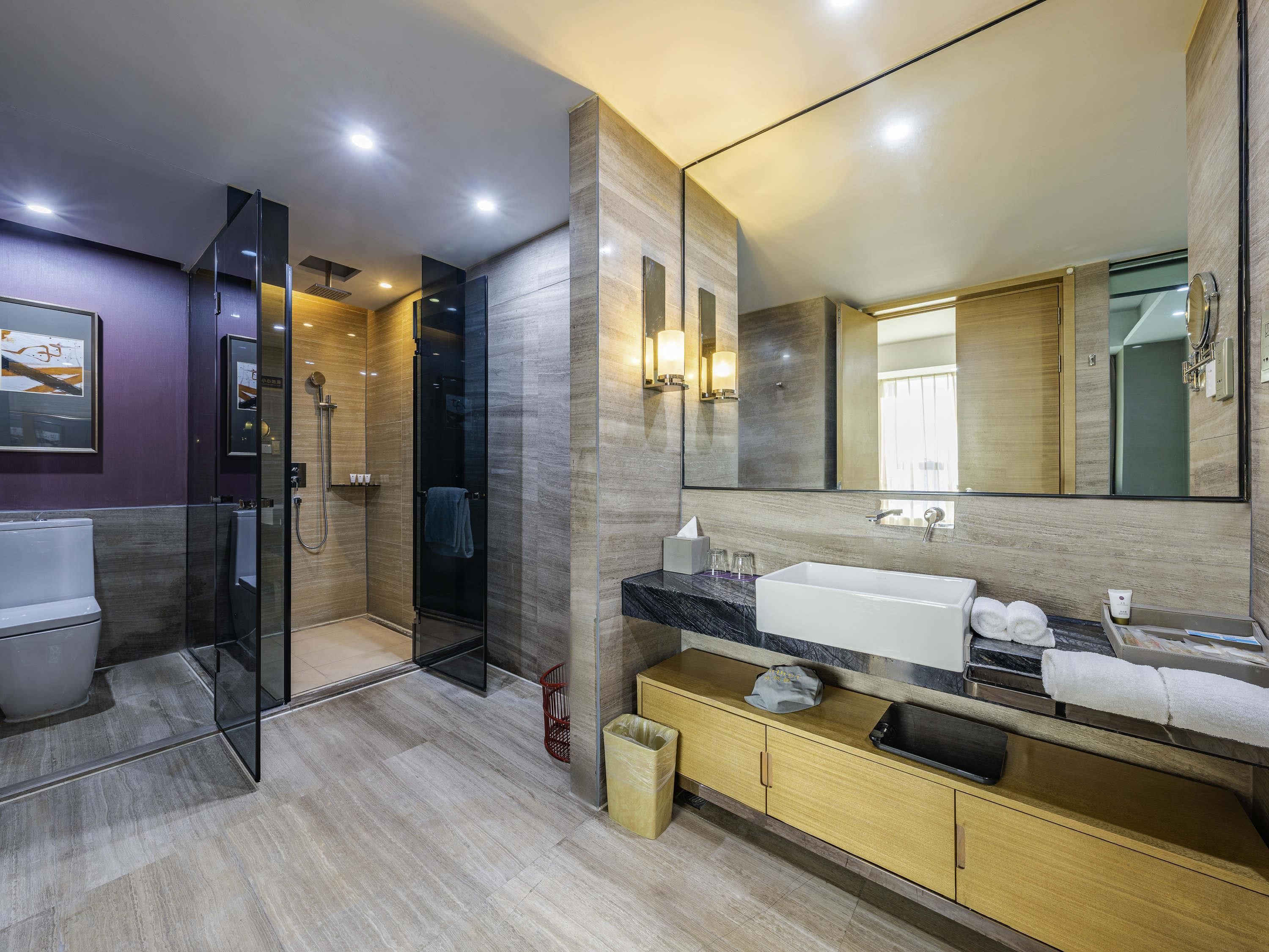 Une salle de bain moderne avec une douche à parois de verre, un grand miroir et un meuble-lavabo doté d’un évier et d’un porte-serviettes.