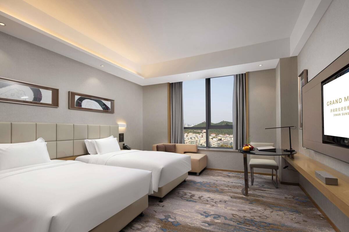 Ein Hotelzimmer mit zwei Betten, einem Schreibtisch, einem Fernseher und Blick auf die Stadt.