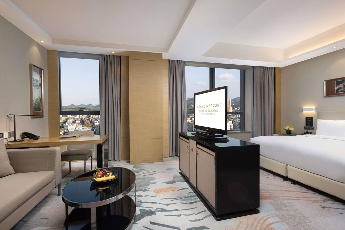 Ein Hotelzimmer mit Bett, Schreibtisch, Stuhl, Couchtisch und Fernseher.