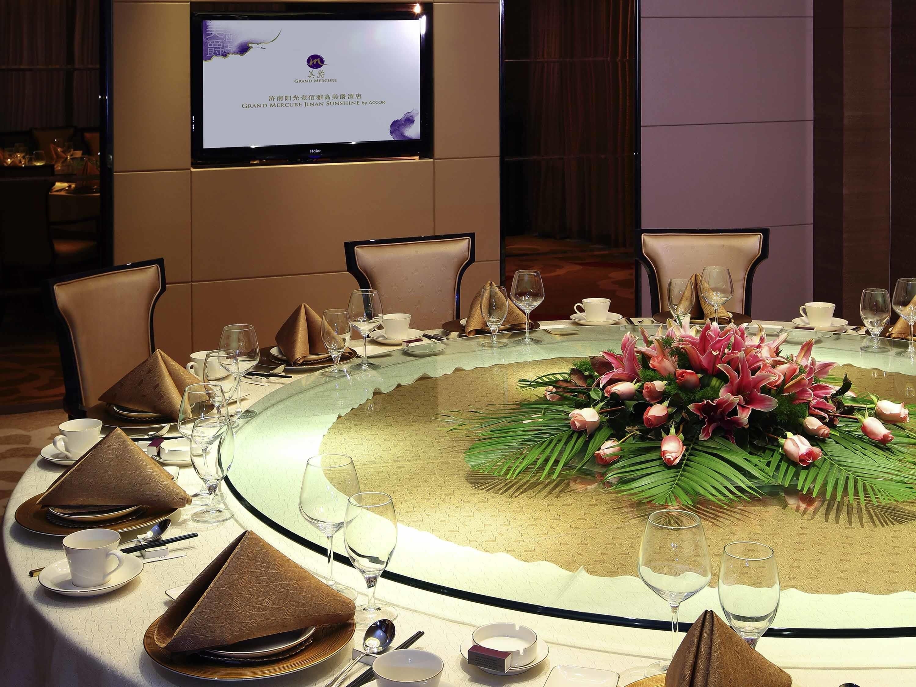 A conference table with a floral centerpiece, surrounded by chairs and diningware.