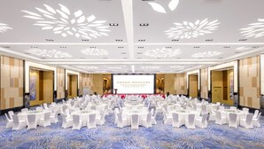 Ein Konferenzraum mit runden Tischen, weißen Stühlen und einer großen Leinwand, auf der „GRAND MERCURY“ angezeigt wird.