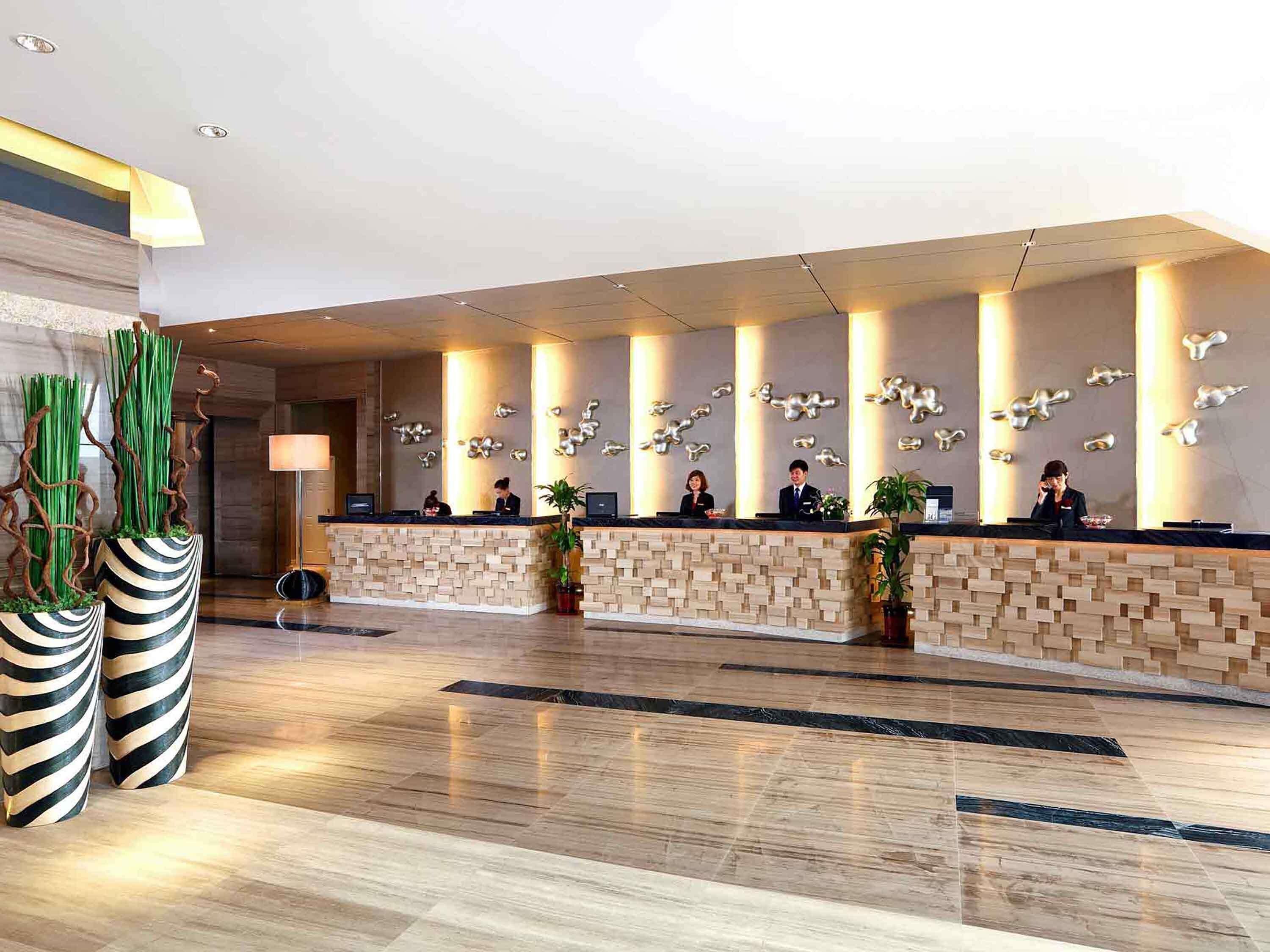A modern hotel reception area with a long counter, several receptionists, and decorative wall art.
