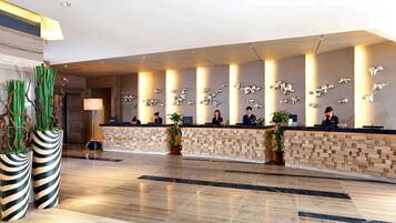 A modern hotel reception area with a long counter, several receptionists, and decorative wall art.
