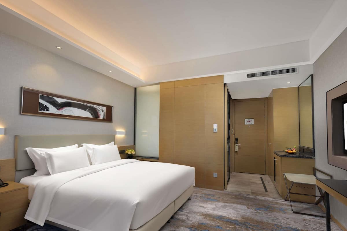 Ein Hotelzimmer mit Bett, Nachttisch, Schreibtisch mit Stuhl, Spiegel und einem Bild an der Wand.