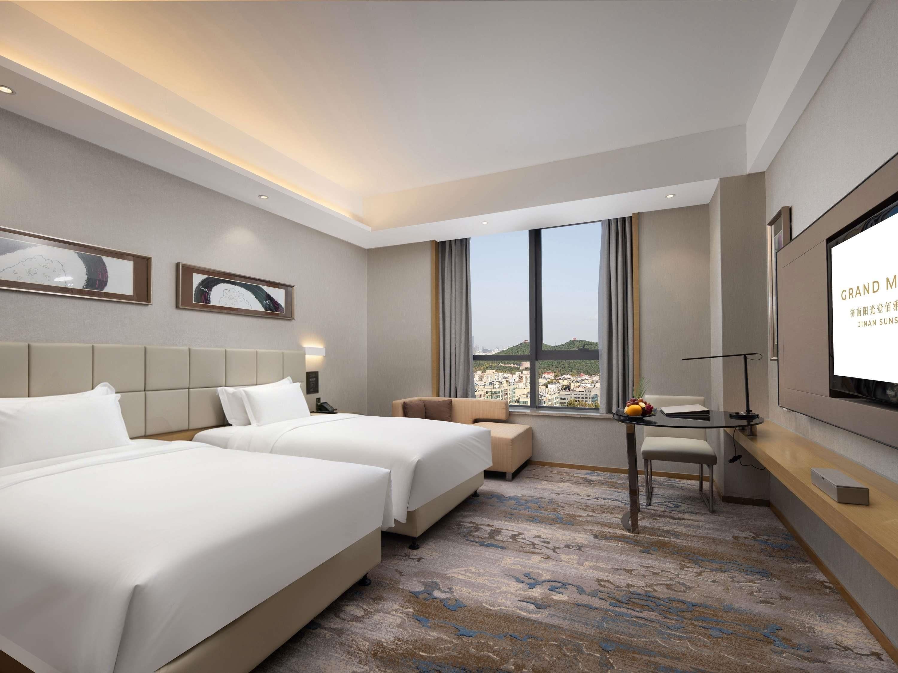 Habitación de hotel con dos camas, un escritorio, un televisor y vistas a la ciudad.