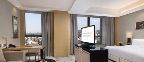 A hotel room with a bed, a desk, a chair, a coffee table, and a TV.