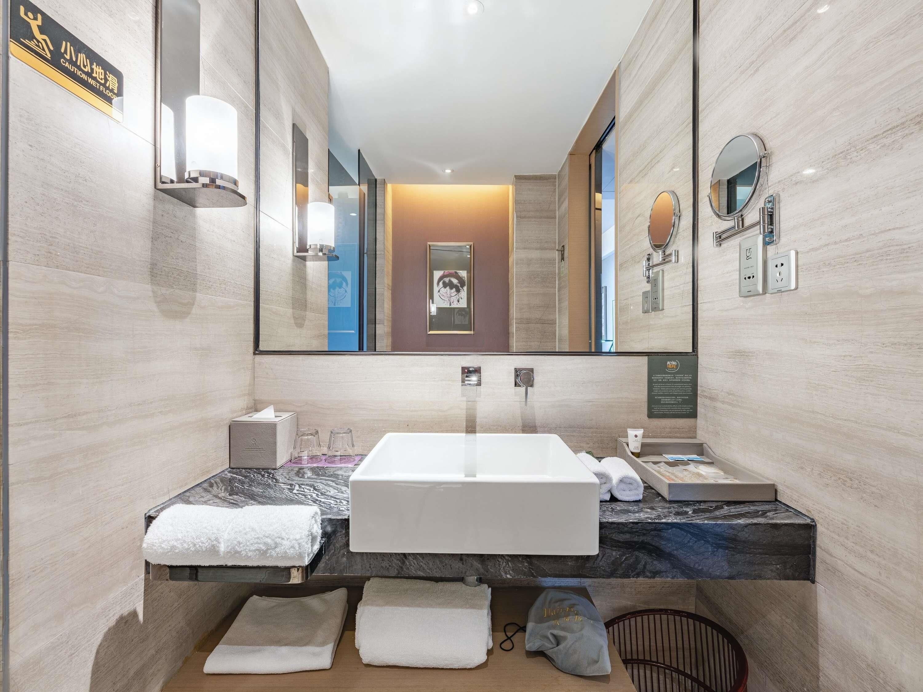 A modern bathroom with a large mirror, a white sink, and a towel rack.