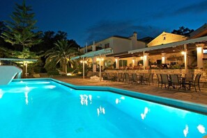 A swimming pool with a covered patio area, stone walls, and outdoor seating. - Paxos Club Resort (Paxos)