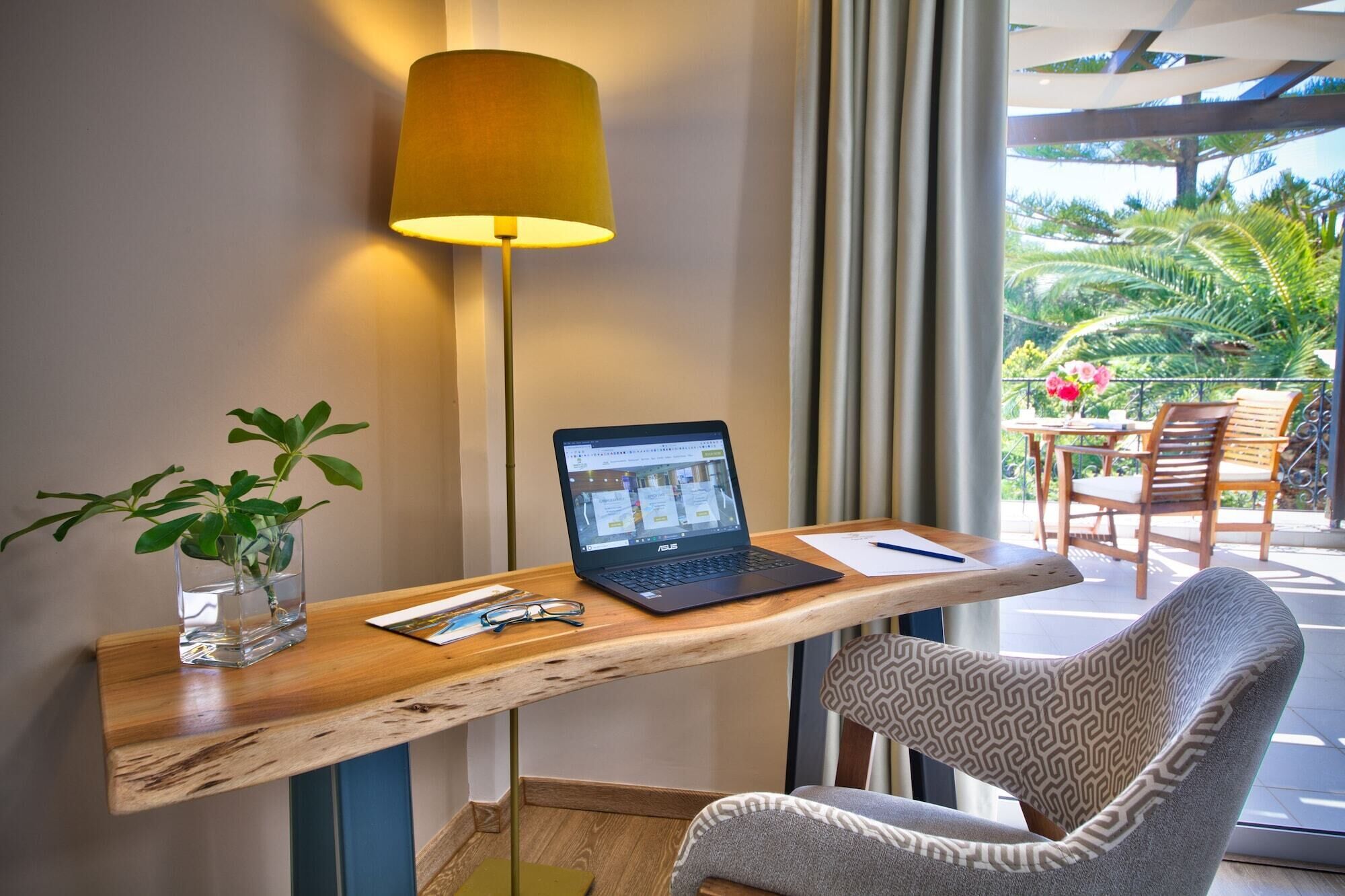 A laptop on a wooden desk with a lamp, a chair, and a plant.