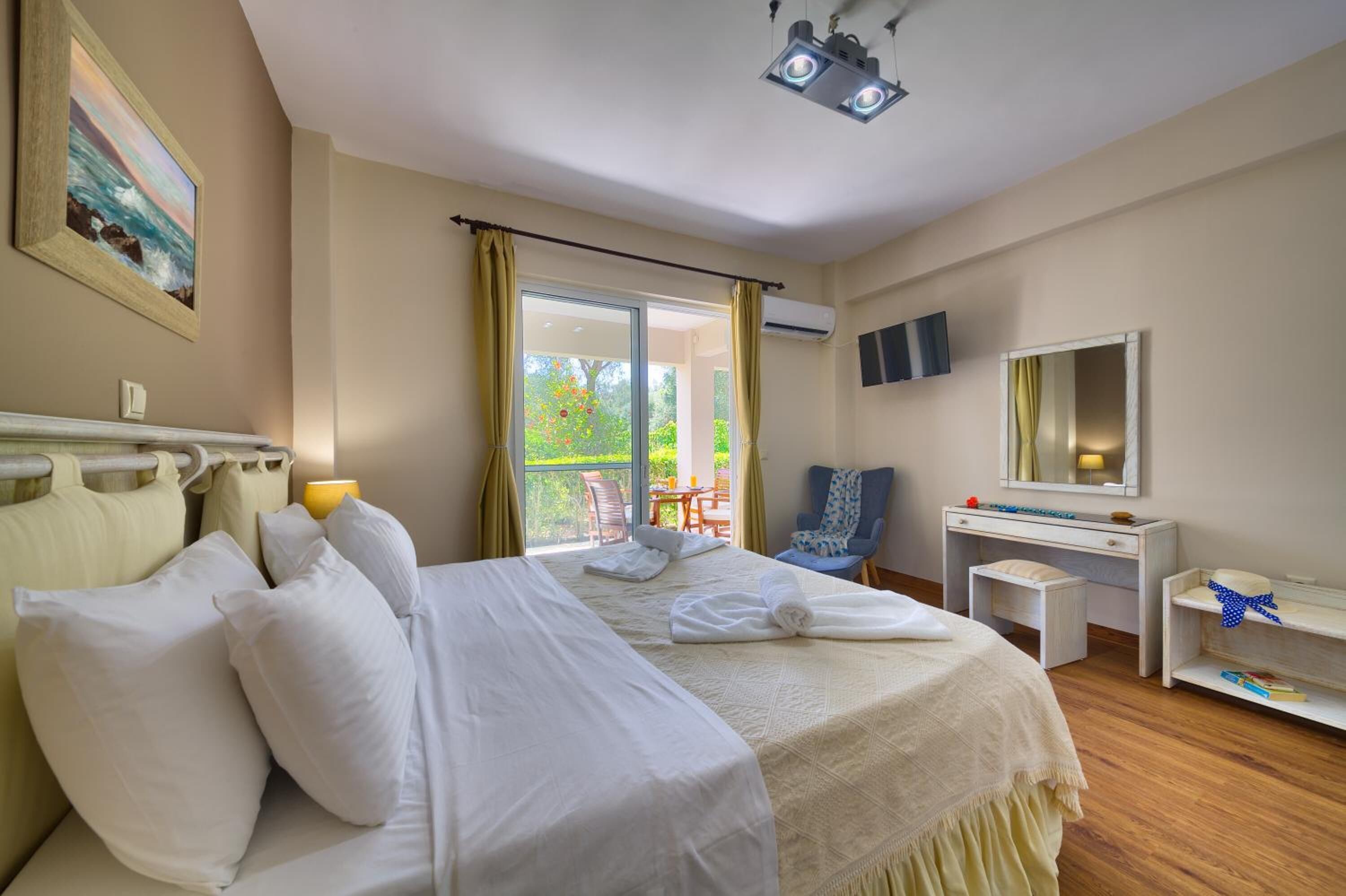 Quarto de hotel com uma cama, escrivaninha, cadeira, mesa pequena, espelho e vista para o exterior.