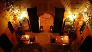 An interior with tables and chairs arranged for dining, a patterned wall, and a door with a decorative element. - Riad La Perle de Marrakech (Marrakech)