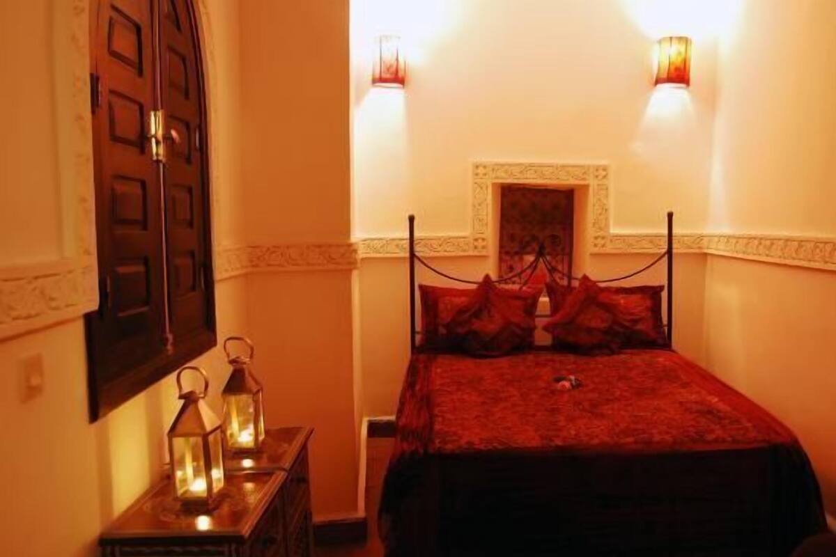 A room with a bed, two wall-mounted lights, and two lanterns on a nightstand.