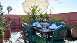 An outdoor dining area with a table set for four, surrounded by green chairs, under a large umbrella. - Riad La Perle de Marrakech (Marrakech)
