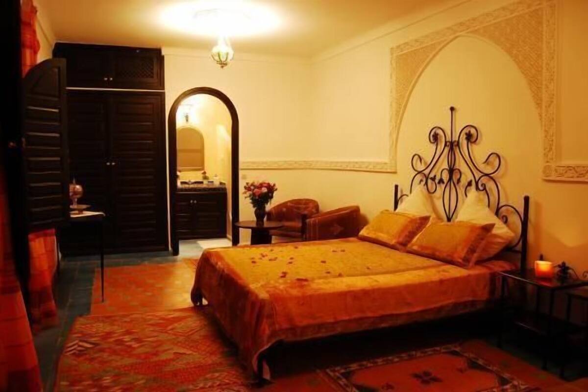 A bedroom with a bed, a nightstand, a mirror, and a door.