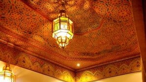 A room with ornate ceiling patterns, a wooden dining table with chairs, and a decorative lamp. - Riad La Perle de Marrakech (Marrakech)