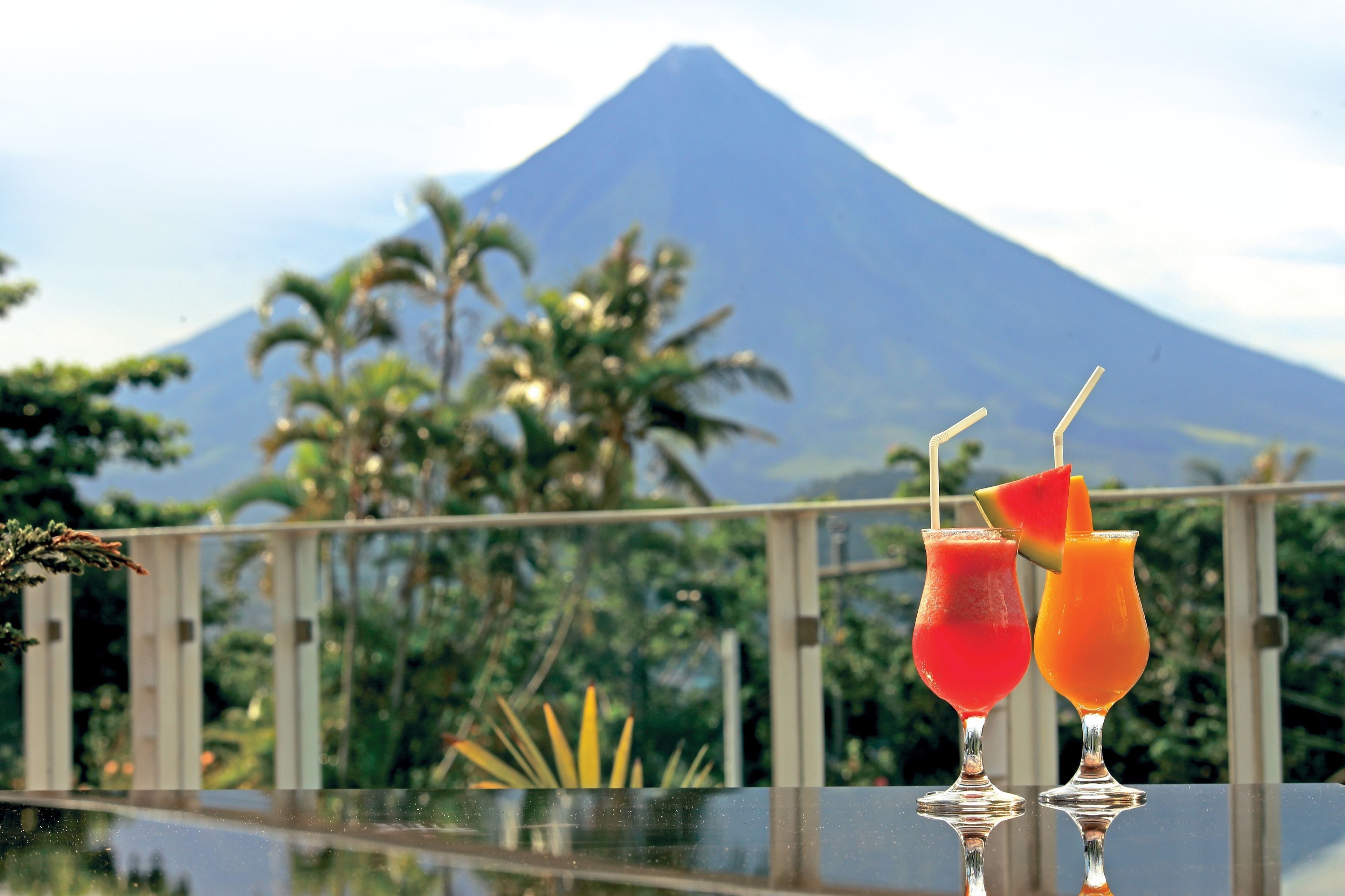 Two drinks on a reflective surface with a mountain in the background.