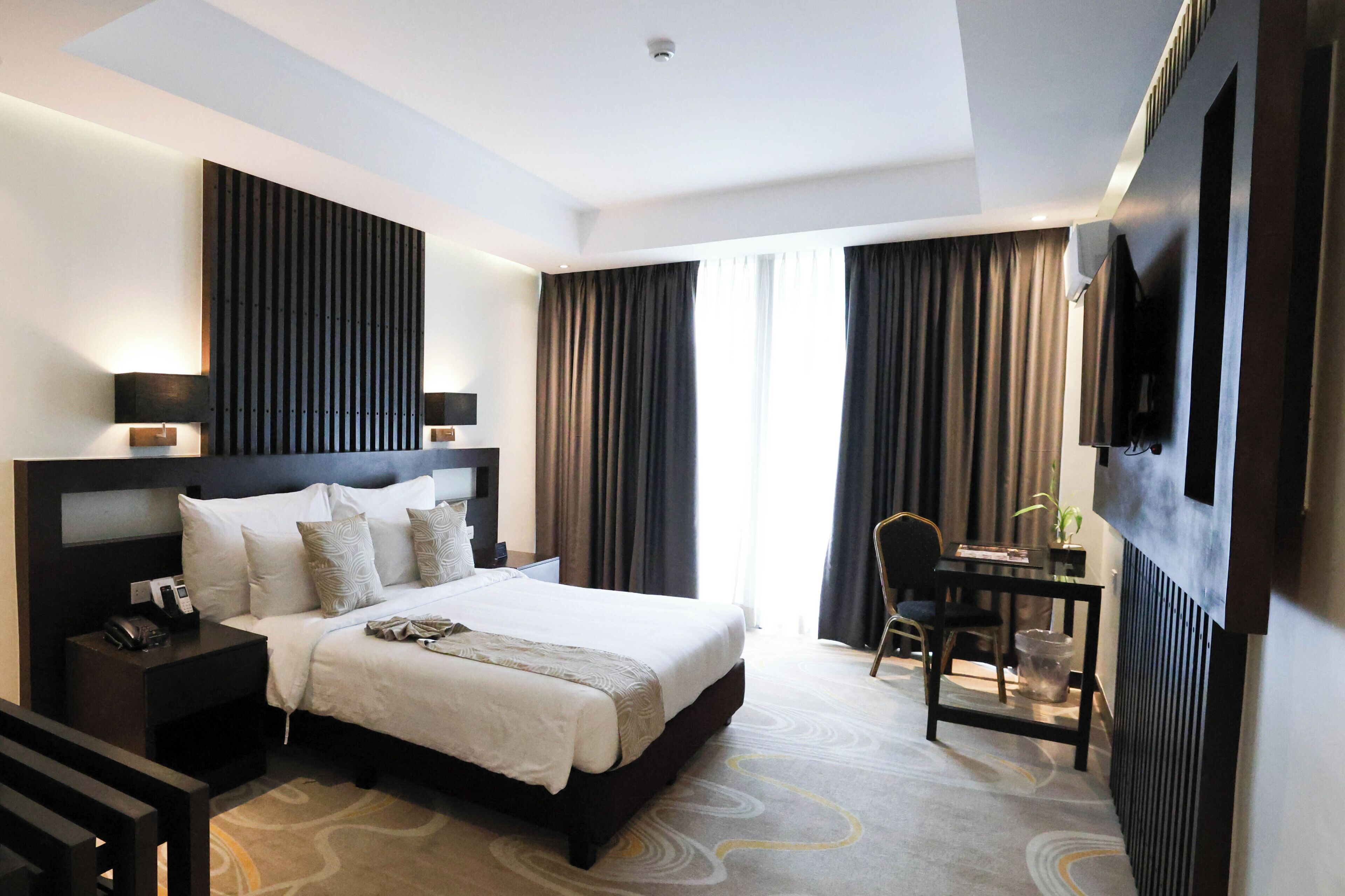 Une chambre d’hôtel moderne, dotée d’un grand lit, de tables de chevet, d’un bureau et d’un téléviseur fixé au mur.