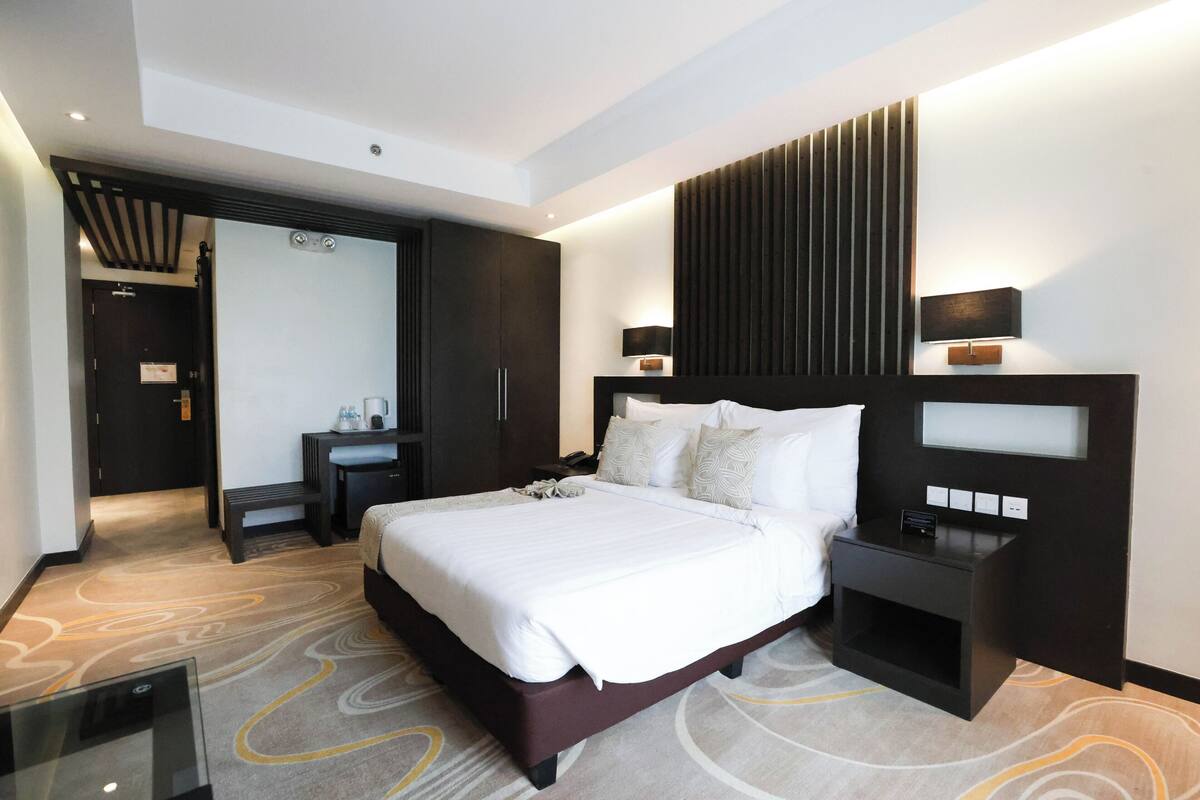Una habitación de hotel moderna con una cama grande, una mesita de noche, un escritorio y un armario.