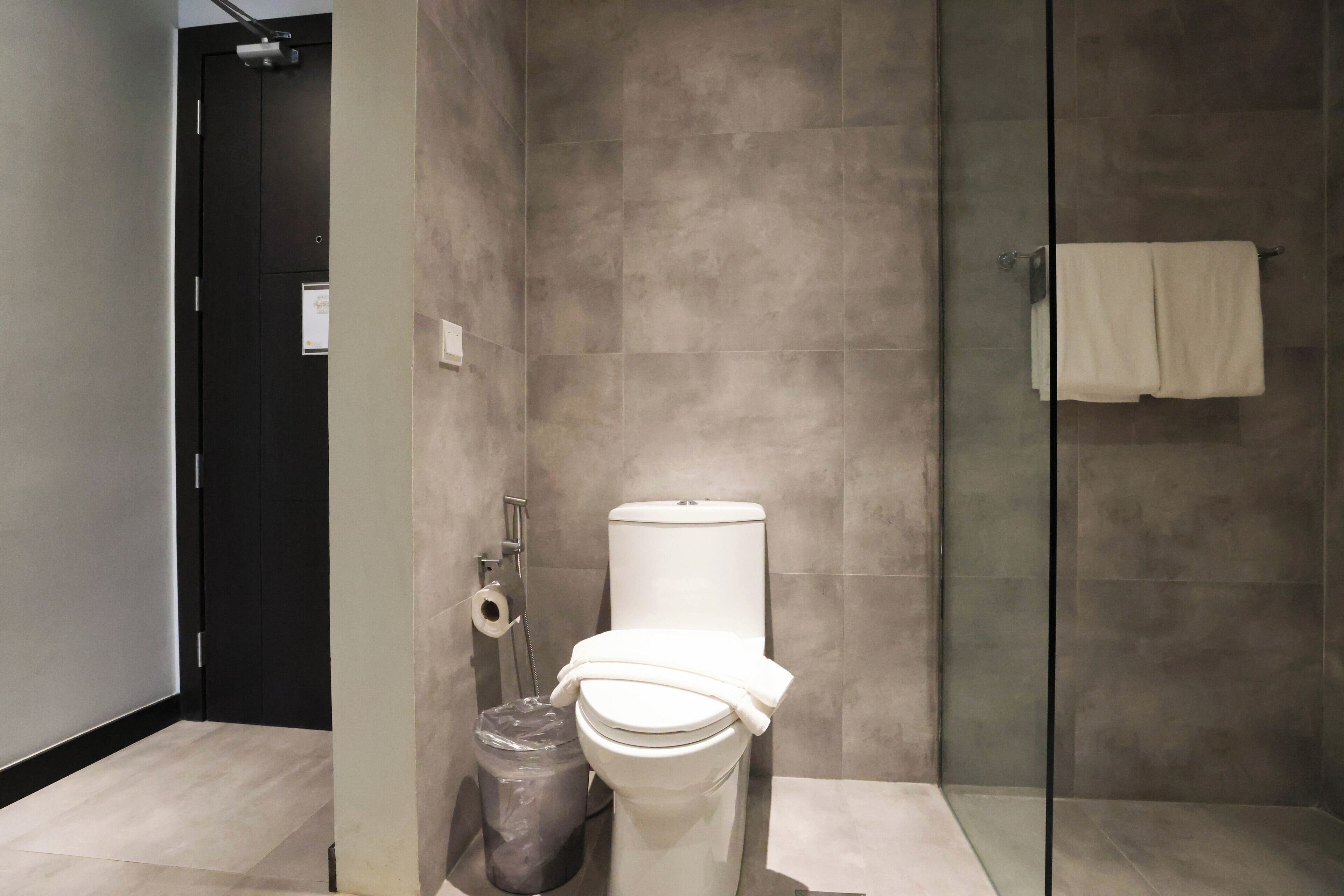 A modern bathroom with a toilet, a trash bin, and a glass shower enclosure.