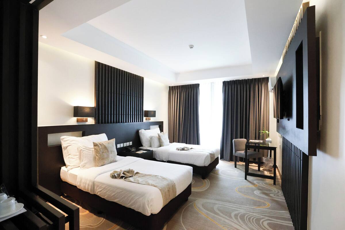Habitación de hotel con dos camas, un escritorio, una silla, un televisor y una ventana con cortinas.